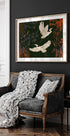 a black and white sofa with a white throw blanket and two white pillows, set against a dark wall with a framed painting of two white birds in flight above it.