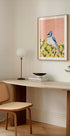 a cozy corner of a room with a wooden desk, a woven chair, a lamp, and a framed picture of a blue bird on a yellow background.